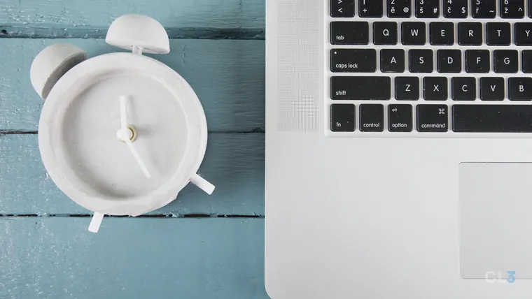 Despertador analógico sobre a mesa, ao lado de um notebook aberto, em close