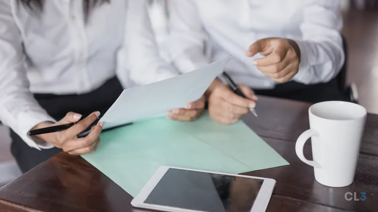Duas pessoas trabalhando lado a lado com documentos sobre a mesa, em close