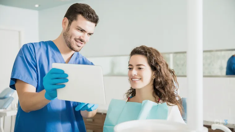 Dentista mostrando a tela de um tablet a uma paciente durante o atendimento na clínica