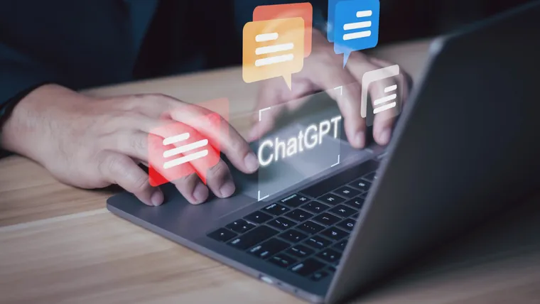 Mãos digitando num notebook com o nome ChatGPT e balões de conversa flutuando sobre o teclado